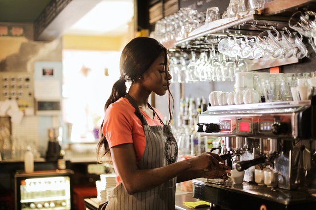 Woman in an apron makes coffee behind a bar